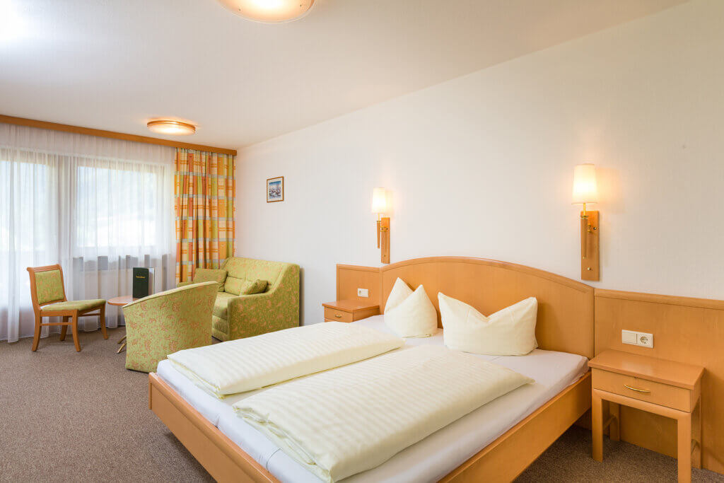 Cozy room in Hotel Grissemann Flirsch with double bed, seating area, and mountain view