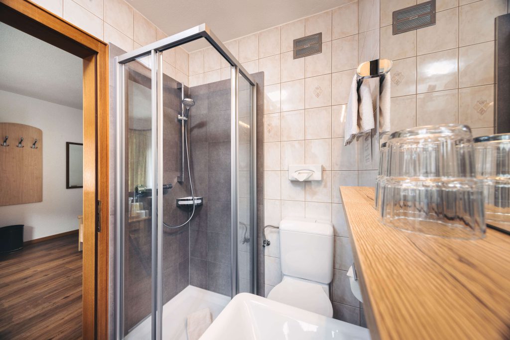 Bright bathroom in Hotel Grissemann Flirsch with shower, toilet, towels and wooden details